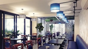 Ein modernes Restaurant mit Tischen, Stühlen, blauen Hängelampen und großen Fenstern.