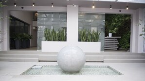 A modern building entrance with a large spherical sculpture in the center, surrounded by potted plants and a glass wall. - Hoang Long Boutique Hotel (Ho Chi Minh City)