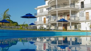 A multi-story hotel with a pool, balconies, and blue umbrellas. - Sea Crest Hotel (Kiwengwa)