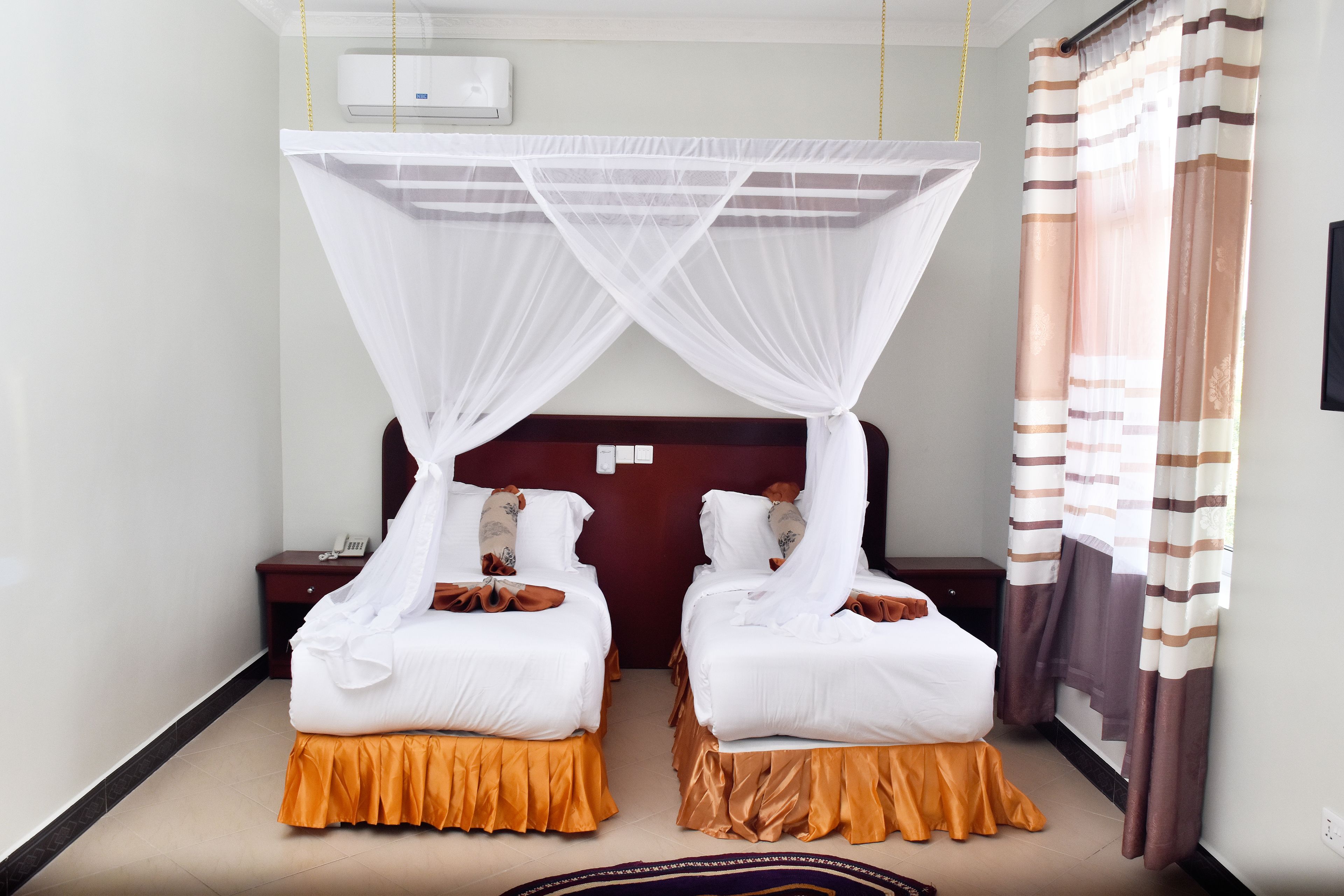 Ein Hotelzimmer mit zwei Betten, jedes mit Baldachin und Holz-Kopfteil. An jedem Bett steht ein Nachttisch mit Lampe und Telefon.