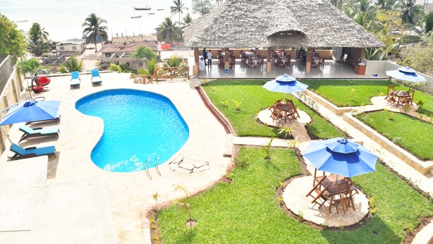 A pool area with a thatched-roof structure, lounge chairs, and umbrellas. - Sea Crest Hotel (Kiwengwa)