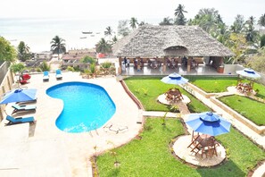 A pool area with a thatched-roof structure, lounge chairs, and umbrellas. - Sea Crest Hotel (Kiwengwa)