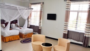 A hotel room with a bed, two chairs, a small table, a TV, and a window with curtains. - Sea Crest Hotel (Kiwengwa)