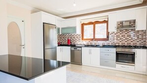 Une cuisine moderne avec des meubles blancs, un plan de travail noir, des appareils en acier inoxydable et un pare-feu décoratif.