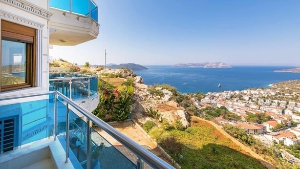 Un bâtiment moderne doté d’un balcon en verre offrant une vue sur une ville côtière et la mer.