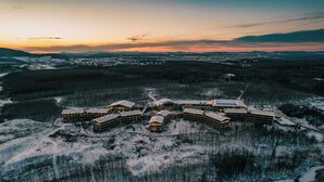 An aerial view of a resort with multiple buildings, surrounded by snow-covered terrain and distant mountains. - Pullman Changbaishan Resort (Baishan)