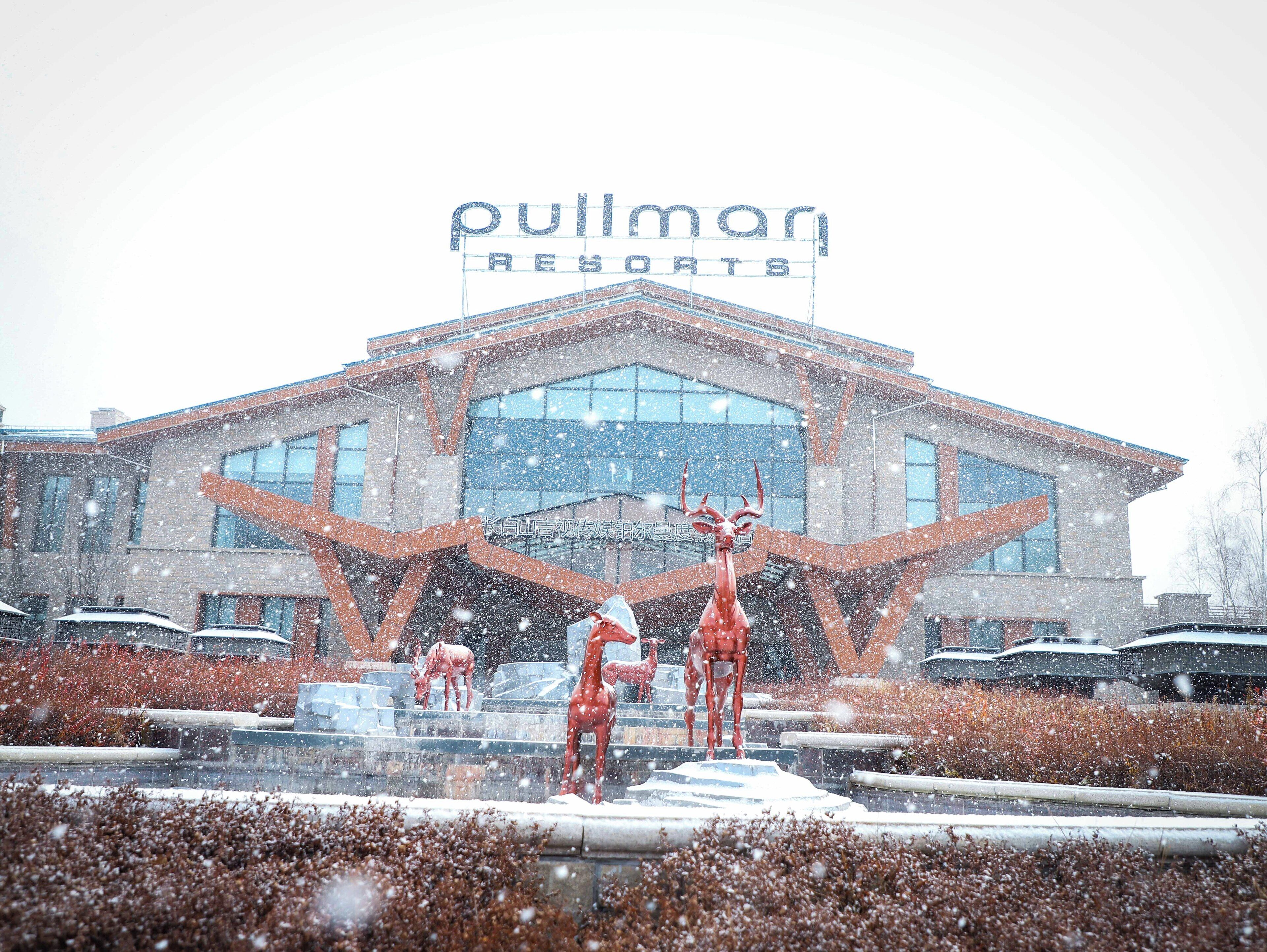 A building with a sign reading 'pullman resorts' and a fountain with deer statues in front.
