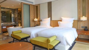 A hotel room with two beds, a sitting area with chairs, a wooden nightstand, and a large mirror. - Pullman Changbaishan Resort (Baishan)