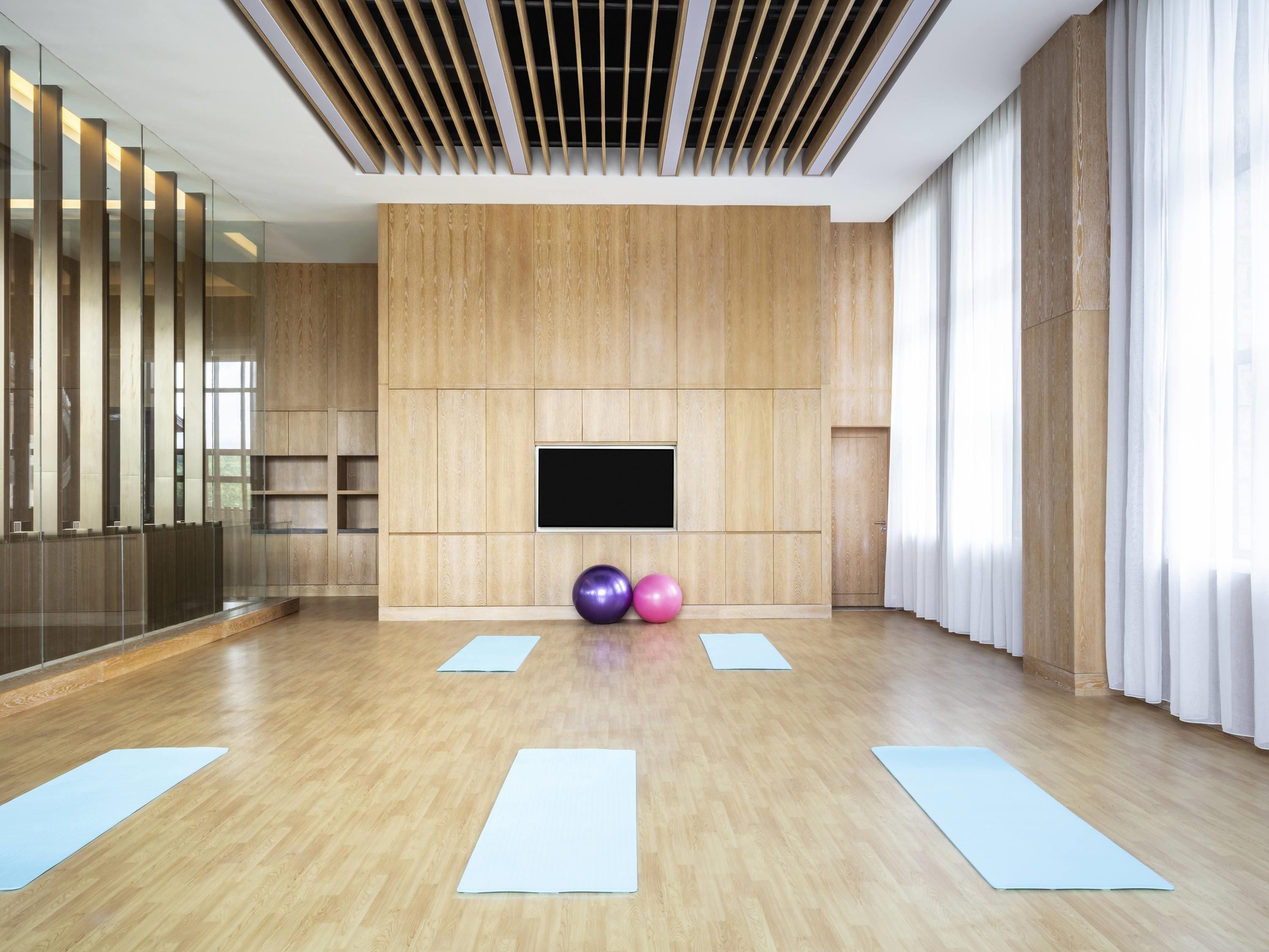 A spacious room with a wooden floor, a mounted TV, and exercise mats.