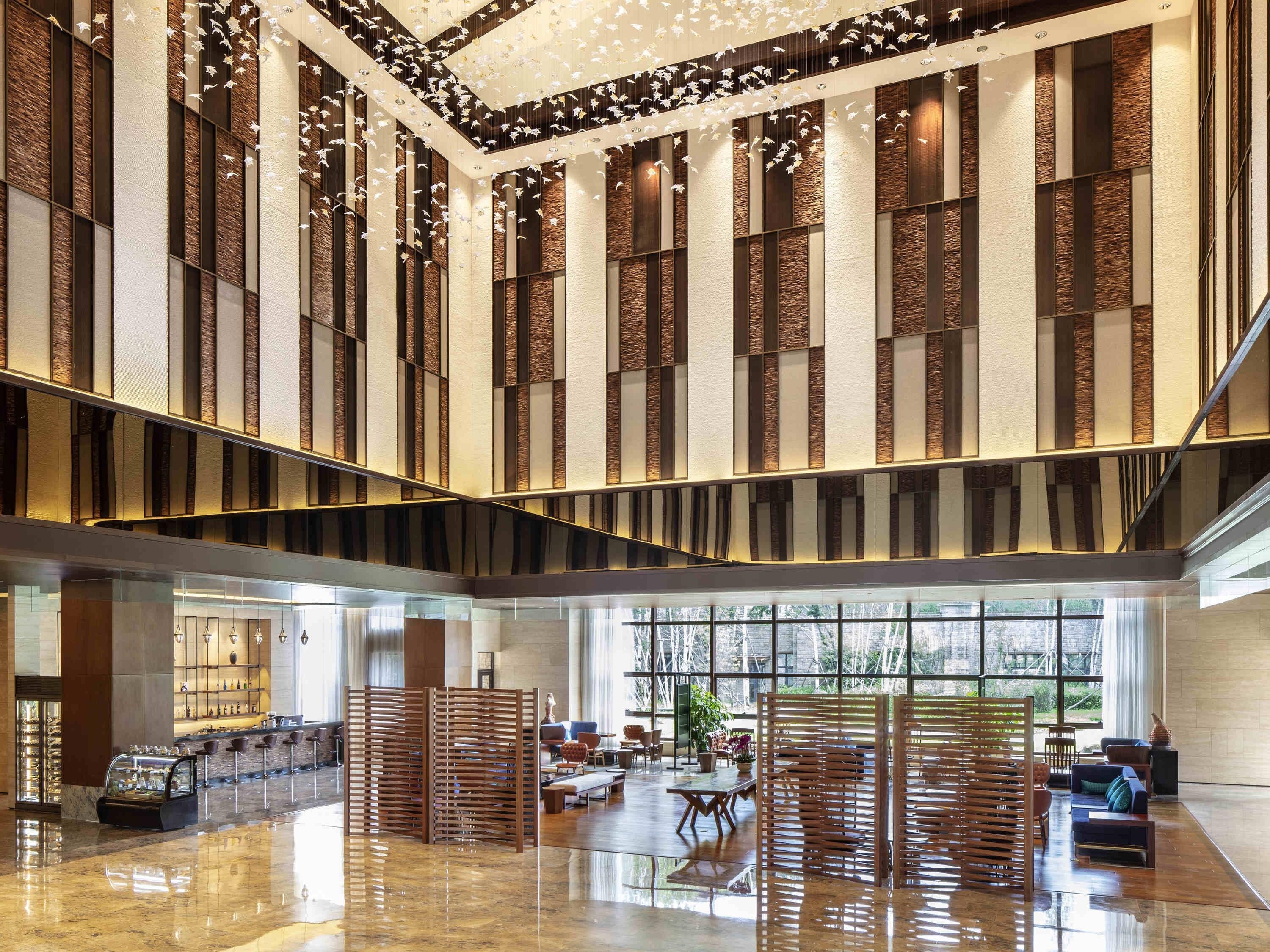 A spacious lobby with a high ceiling, a central staircase, and a seating area with tables and chairs.