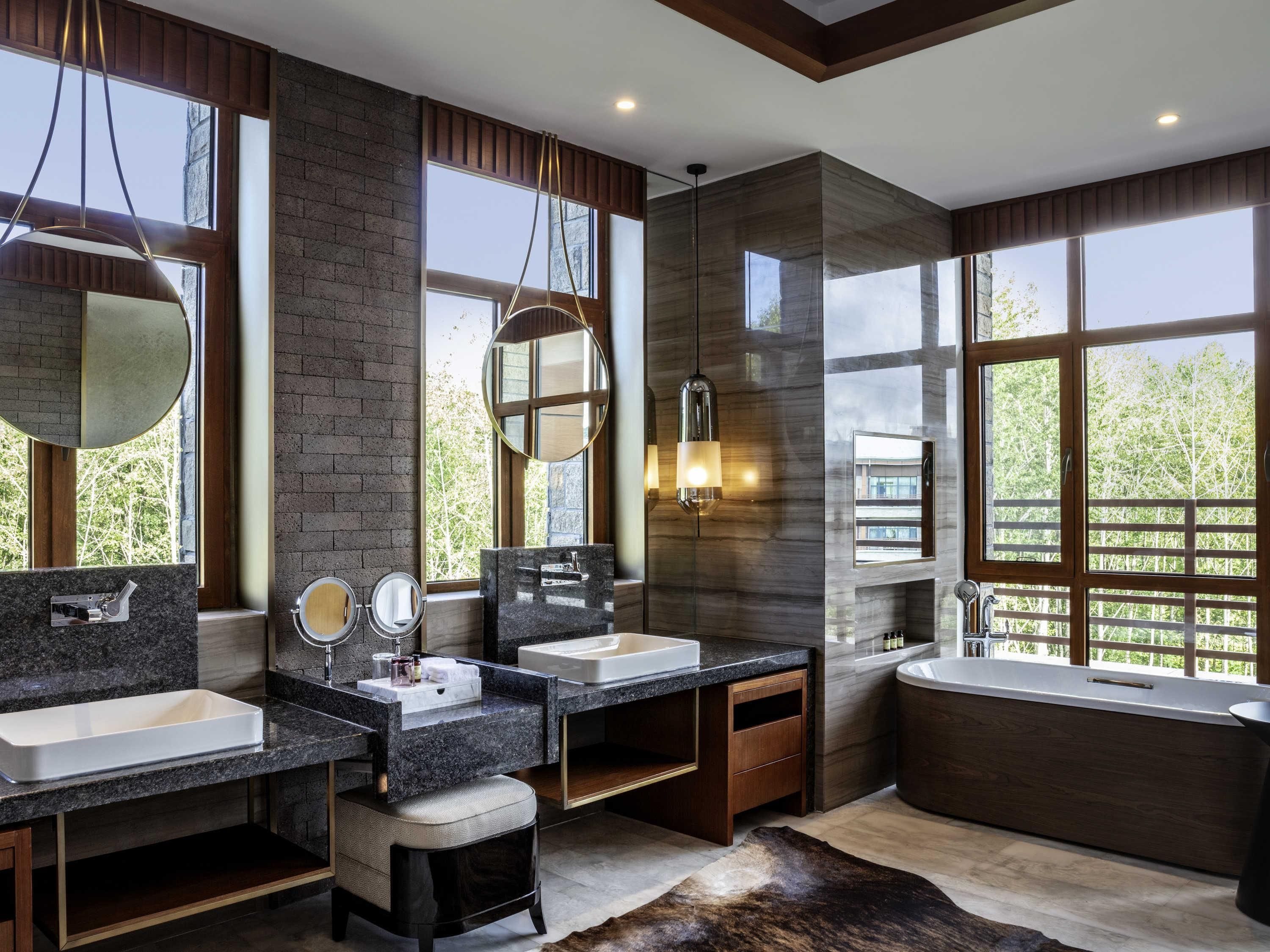 Un bagno moderno con due lavabi, uno specchio grande, una vasca da bagno e ampie finestre.
