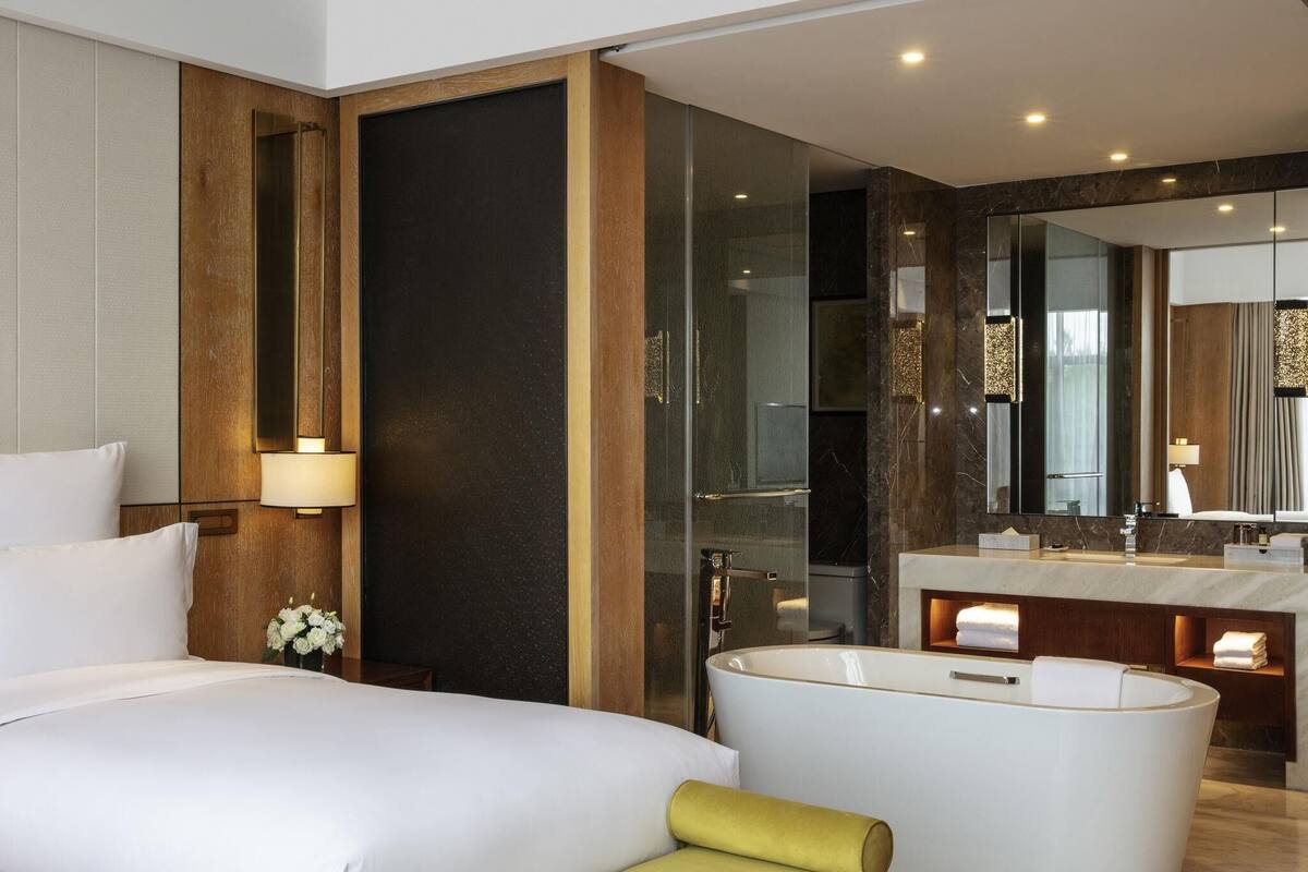 Een moderne hotelkamer met een groot bed, een badkuip, een wastafel met spiegel en een wandlamp.