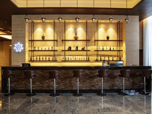 A bar area with a marble countertop, multiple shelves with bottles, and bar stools. - Pullman Changbaishan Resort (Baishan)