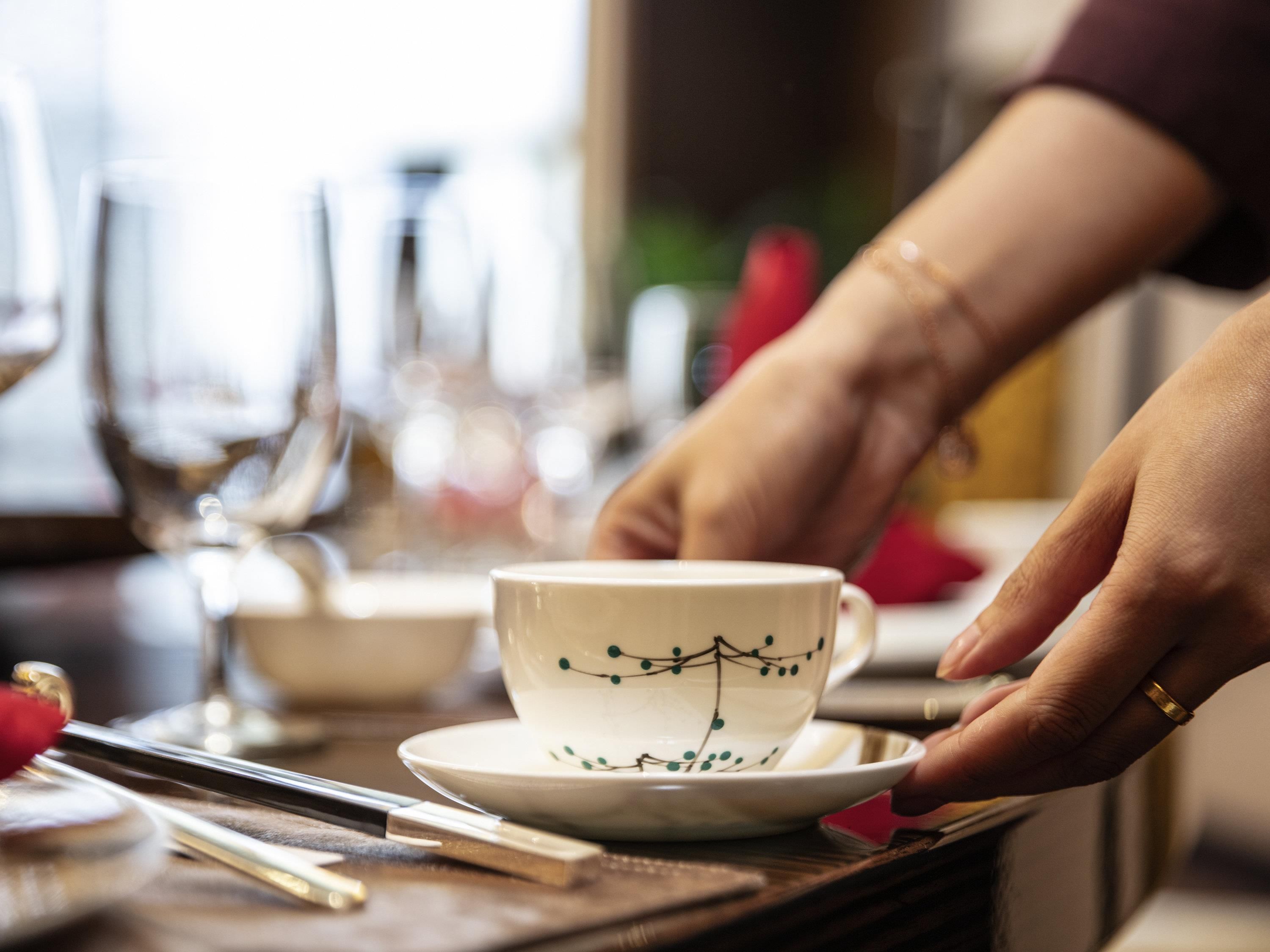 A hand placing a cup on a saucer.