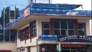 A hotel with a blue awning, a sign indicating it is a hotel, and a view of a modern building in the background.