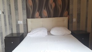 A hotel room with a large bed, two white pillows, a folded white towel, and a headboard with a leaf pattern.