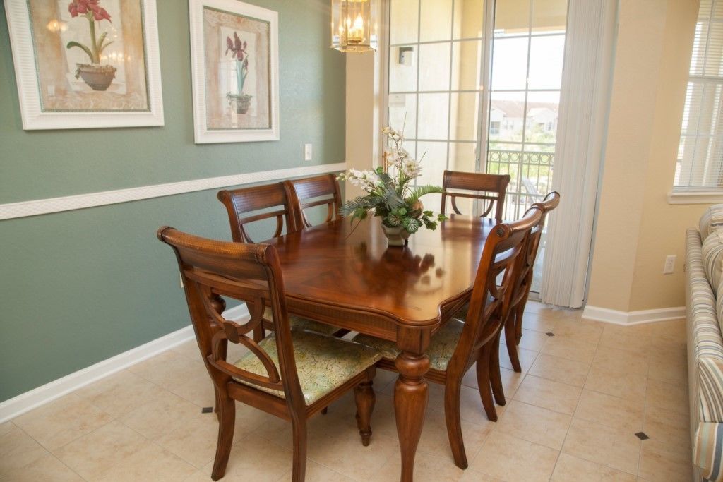 A dining room with a wooden table and chairs, framed artwork on the wall, and a window with blinds.