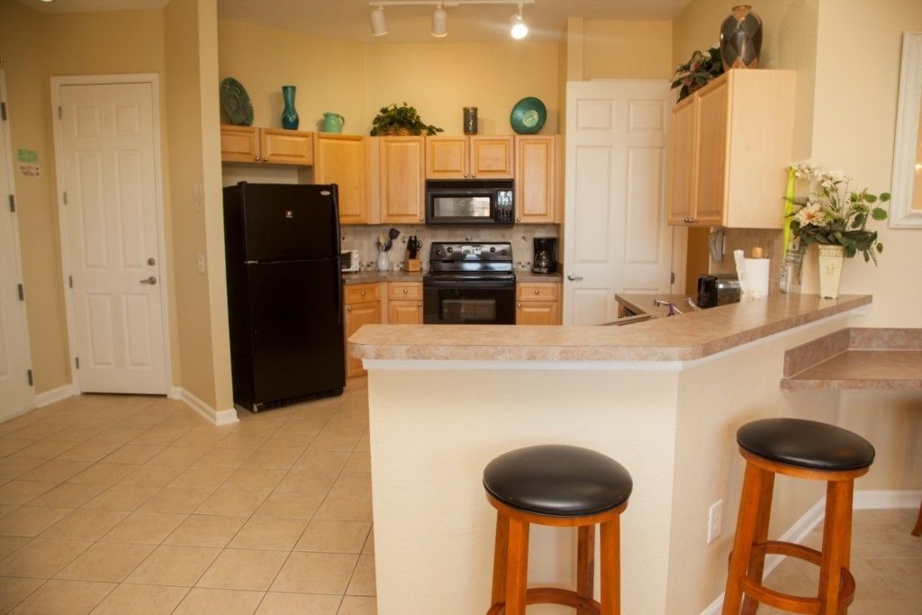 A kitchen with wooden cabinets, a black refrigerator, a stove, and a microwave. There are two stools at the counter.