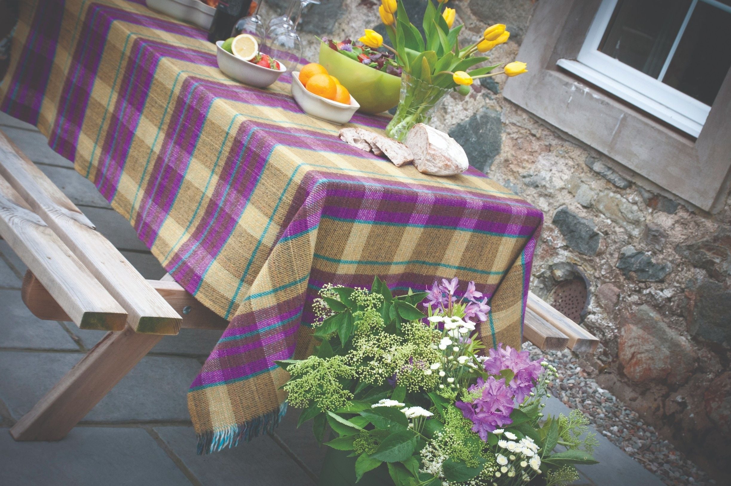 A table set with a plaid tablecloth, a bowl of oranges, a vase of tulips, and a bouquet of flowers.