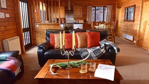 A cozy cabin interior with a leather sofa, a wooden dining table, and a kitchen area. - Leny Estate (Callander)