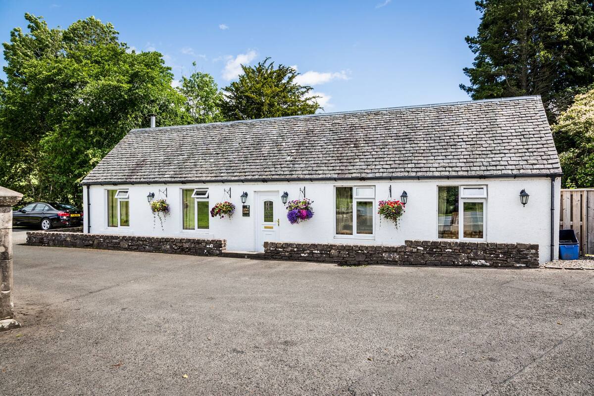 A white building with a stone foundation, multiple windows, and hanging flower baskets.