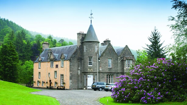 A large, historic building with a prominent tower and multiple chimneys, surrounded by lush green lawns and a cobblestone driveway. - Leny Estate (Callander)