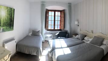 A bedroom with two beds, a radiator, a desk, a chair, a lamp, a window, and a painting of a forest.