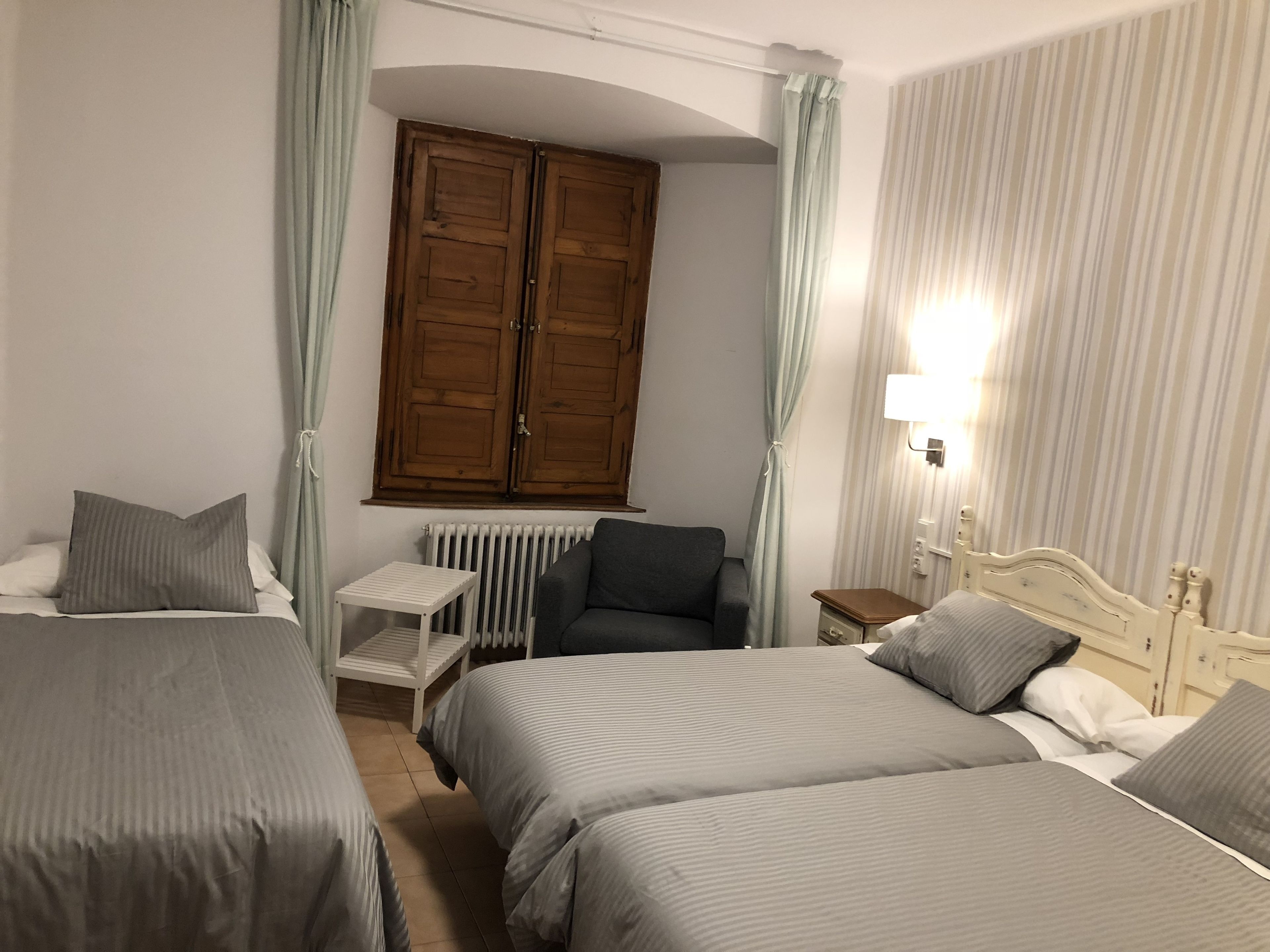 Une chambre d’hôtel avec deux lits simples, une petite table, une chaise, un radiateur et une armoire.
