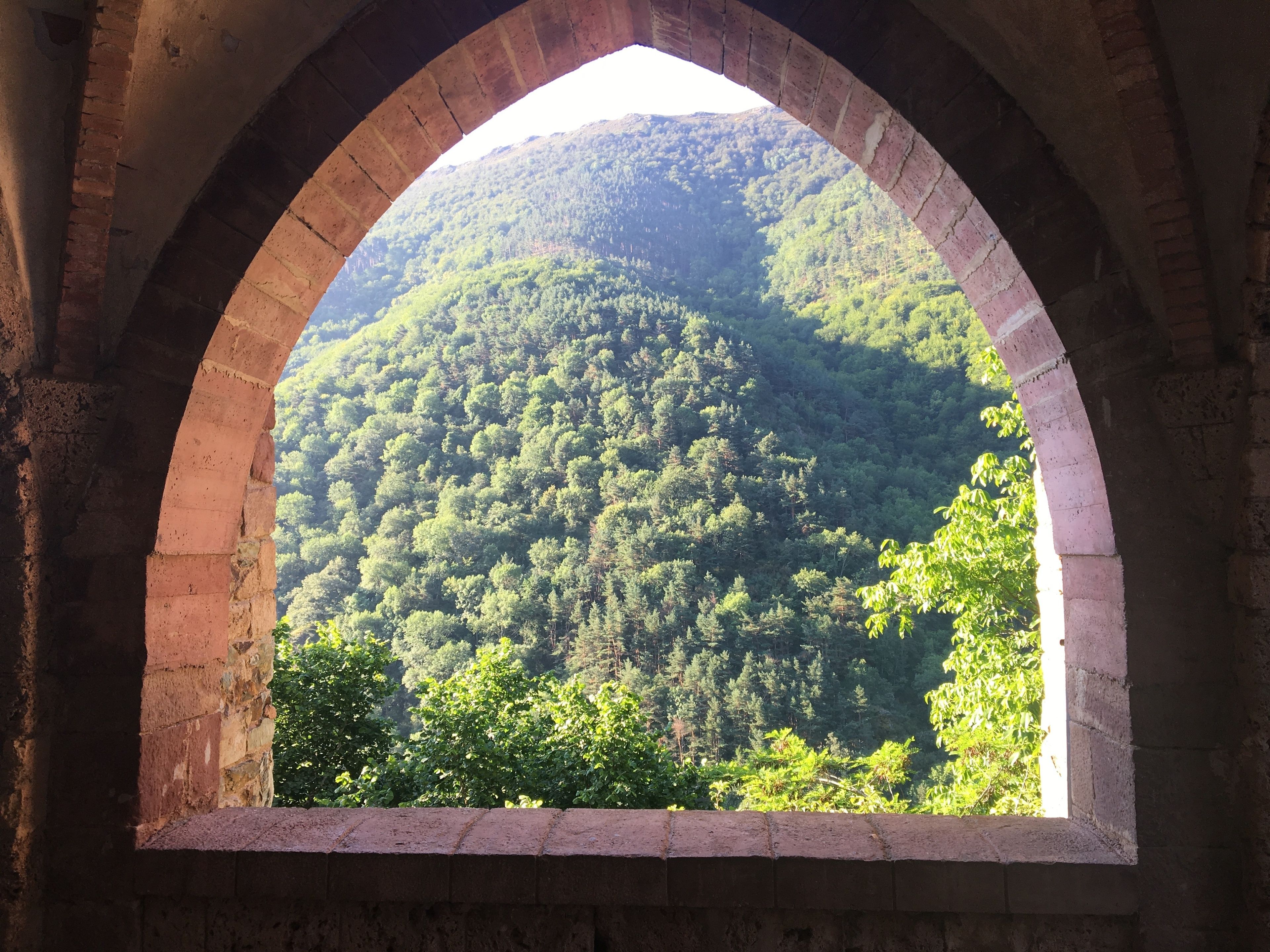 A stone archway with a view of a forested hillside.