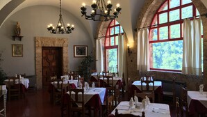 Un restaurant doté de grandes fenêtres en arc, de tables en bois et de lustres.