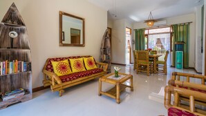A living room with a sofa, a coffee table, a bookshelf, and a dining area with a table and chairs. - Bali Relax and Comfort (Karangasem)
