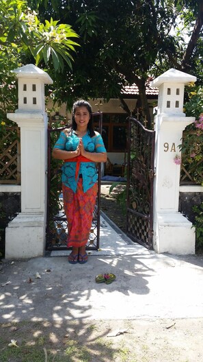 A person standing at a gate with a number plaque, surrounded by greenery and a building in the background. - Bali Relax and Comfort (Karangasem)