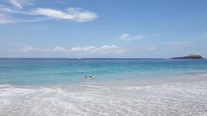 A beach with clear blue water, a distant island, and a few people swimming. - Bali Relax and Comfort (Karangasem)