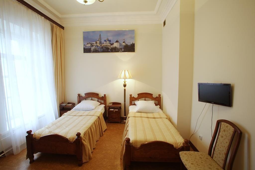 A hotel room with two single beds, a nightstand, a lamp, a television, and a chair.