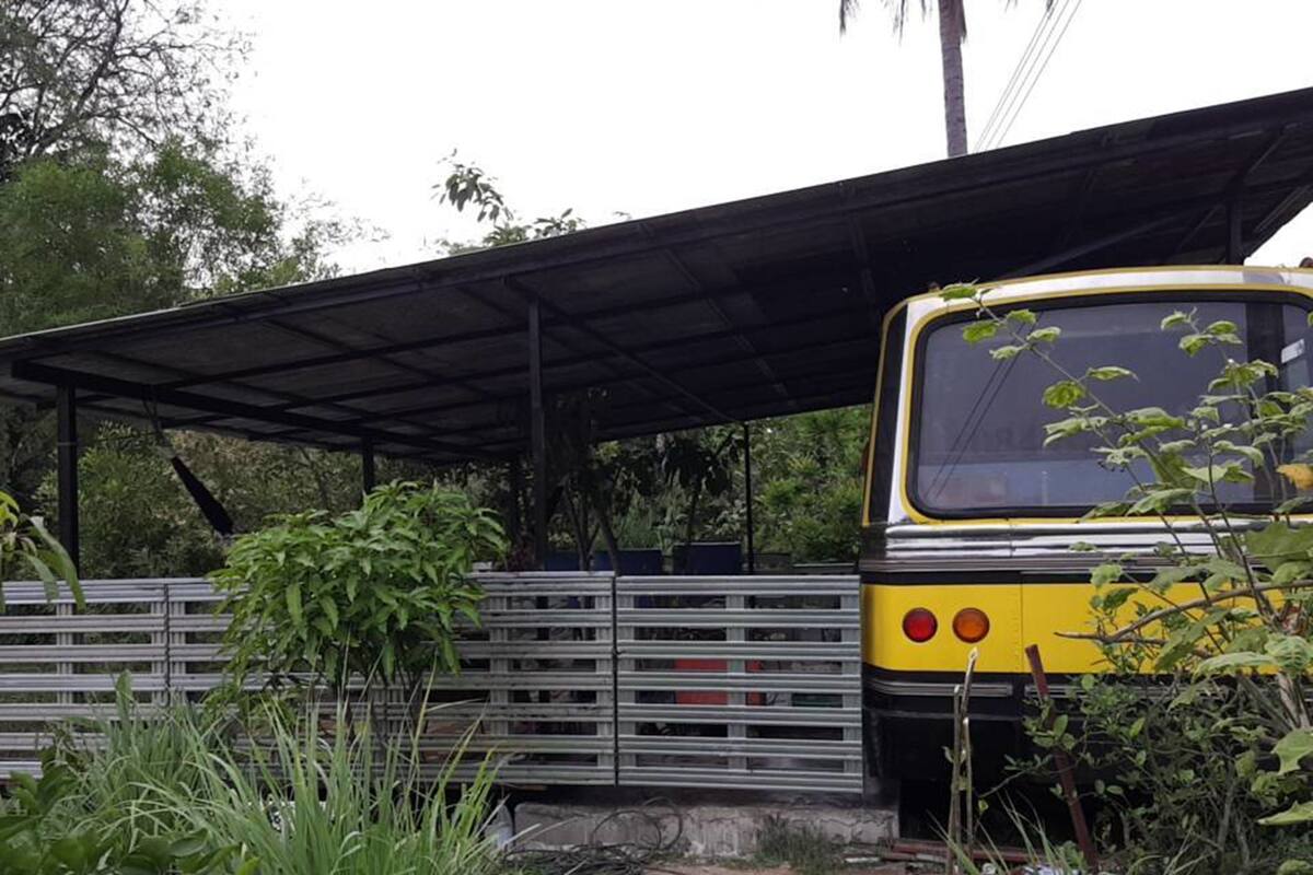 Un autobus jaune était garé sous un abri couvert, agrémenté de garde-corps en métal et entouré de verdure.