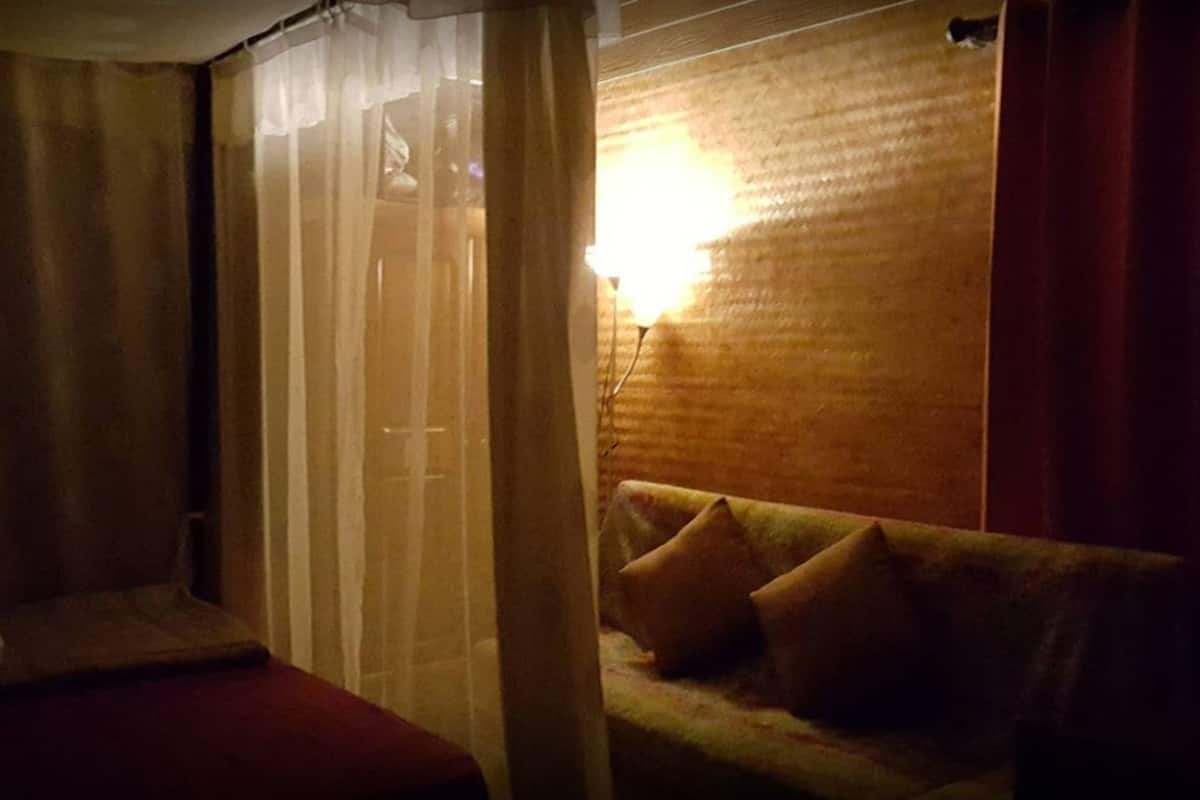 Une pièce faiblement éclairée, avec un canapé, une lampe et un rideau.