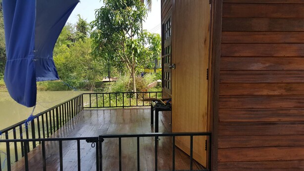 A wooden building with a balcony overlooking a body of water and greenery. - Baan Aunjai Homestay (Mae Lao)