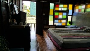 A room with a bed, a television, and a window with colorful panes. - Baan Aunjai Homestay (Mae Lao)