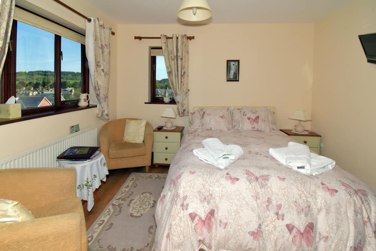 A bedroom with a large bed, a chair, a small table, and a window with curtains.