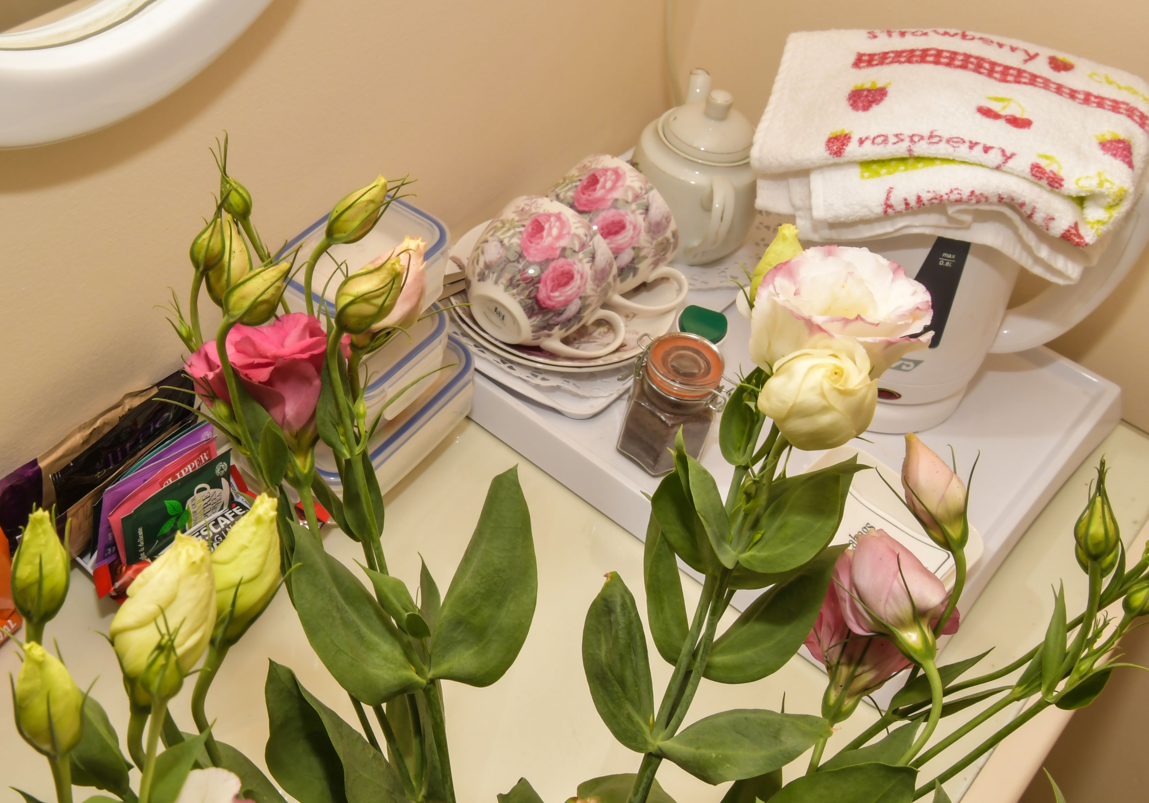 A kitchen counter with a tea set, a jar of jam, and a bouquet of flowers.