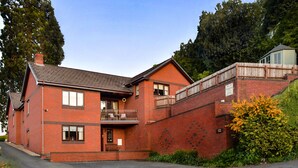 A two-story brick house with a balcony, a fenced yard, and a small shed. - Erris Villa (Builth Wells)