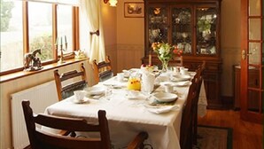 A dining room with a table set for four, a wooden cabinet with glass doors, and a window with curtains. - Erris Villa (Builth Wells)