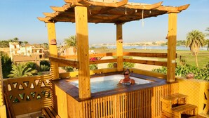 A wooden hot tub with a wooden pergola overhead, surrounded by a wooden fence and steps leading up to it. - Jewel Howard Carter Hotel (Luxor)