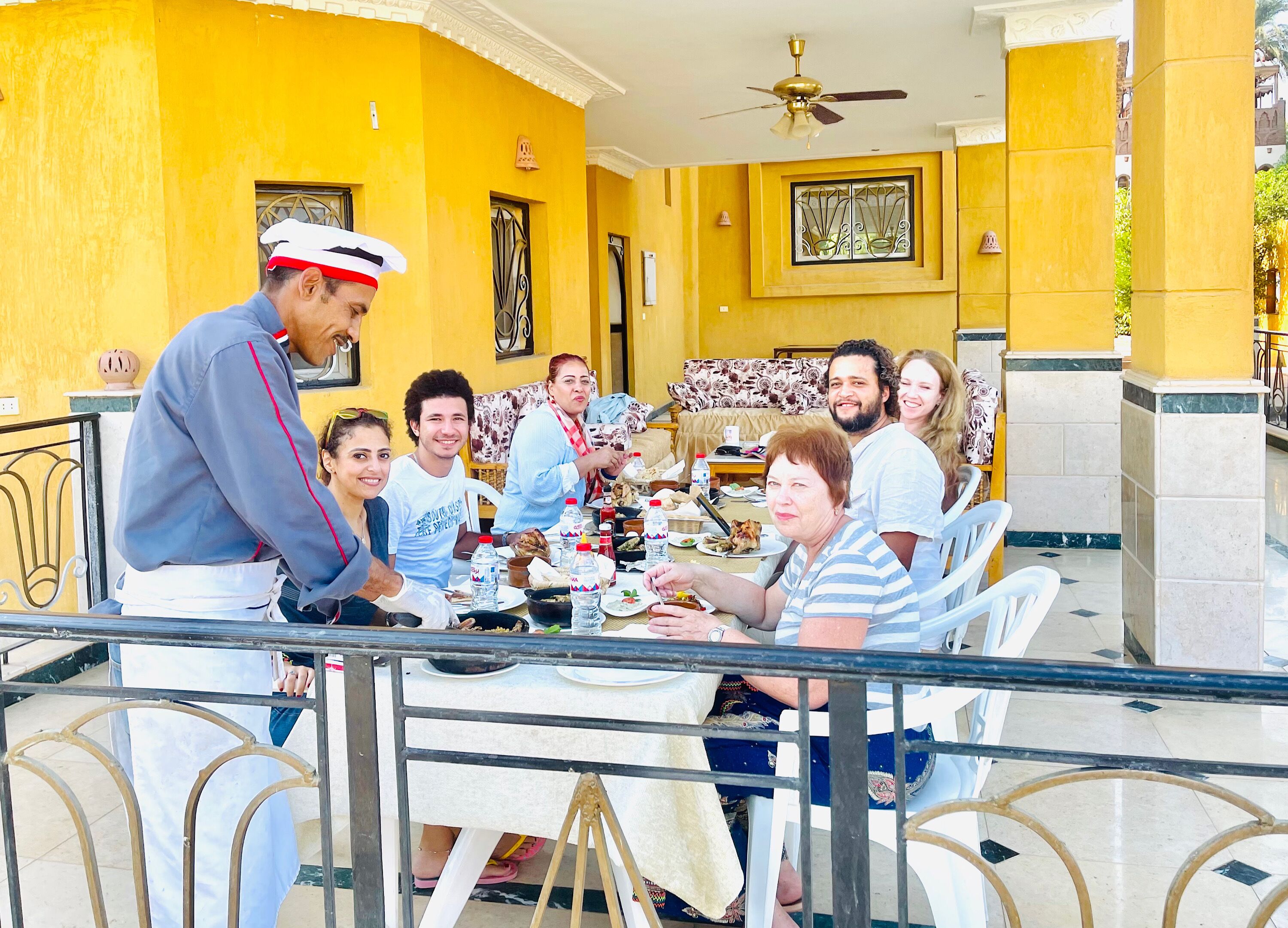 Un grupo de personas cenando en una mesa, con paredes amarillas y un ventilador de techo.
