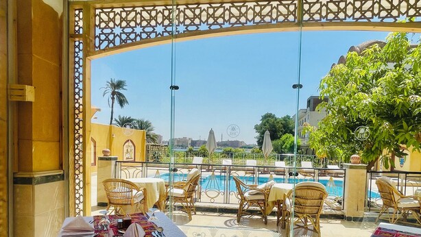 A terrace with wicker furniture, a pool, and a view of the cityscape. - Jewel Howard Carter Hotel (Luxor)