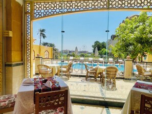 A terrace with wicker furniture, a pool, and a view of the cityscape. - Jewel Howard Carter Hotel (Luxor)