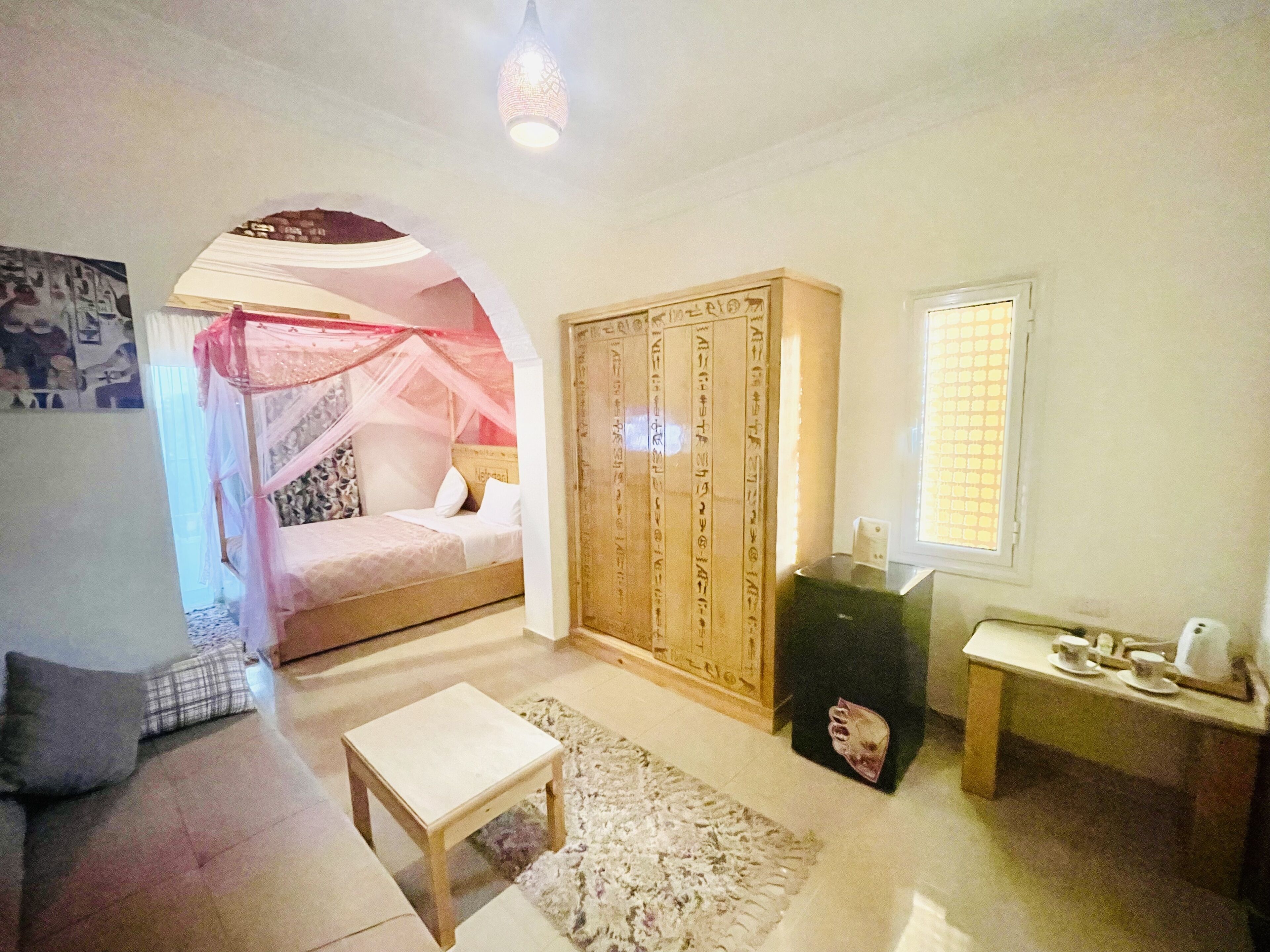 Un dormitorio con cama bajo dosel, armario, mesita y ventana con persianas.
