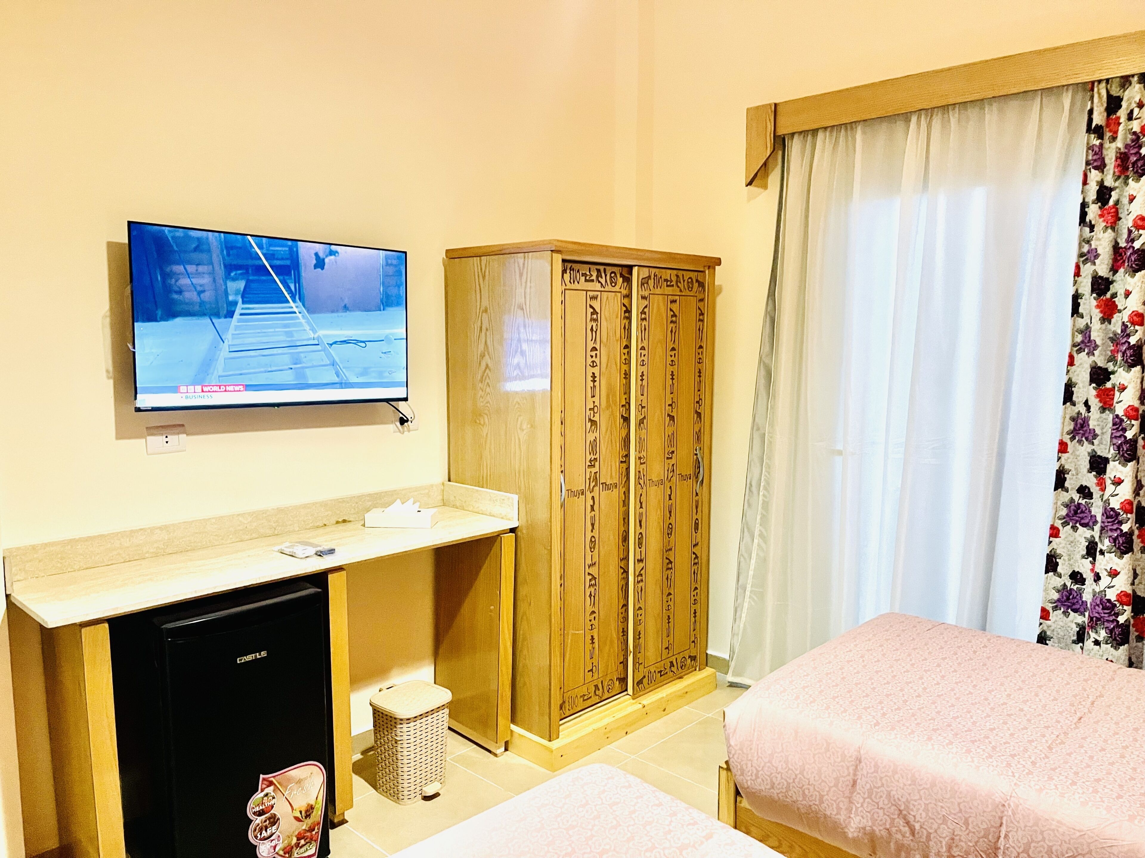 A hotel room with a television, wooden wardrobe, two beds, and a small refrigerator.