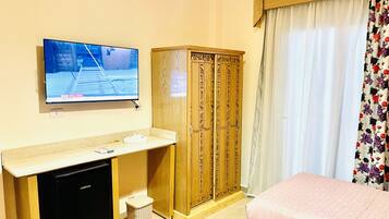 A hotel room with a television, wooden wardrobe, two beds, and a small refrigerator.