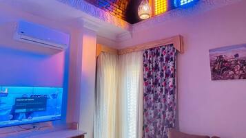 A living room with a flat-screen TV, a sofa, a coffee table, and a patterned curtain.